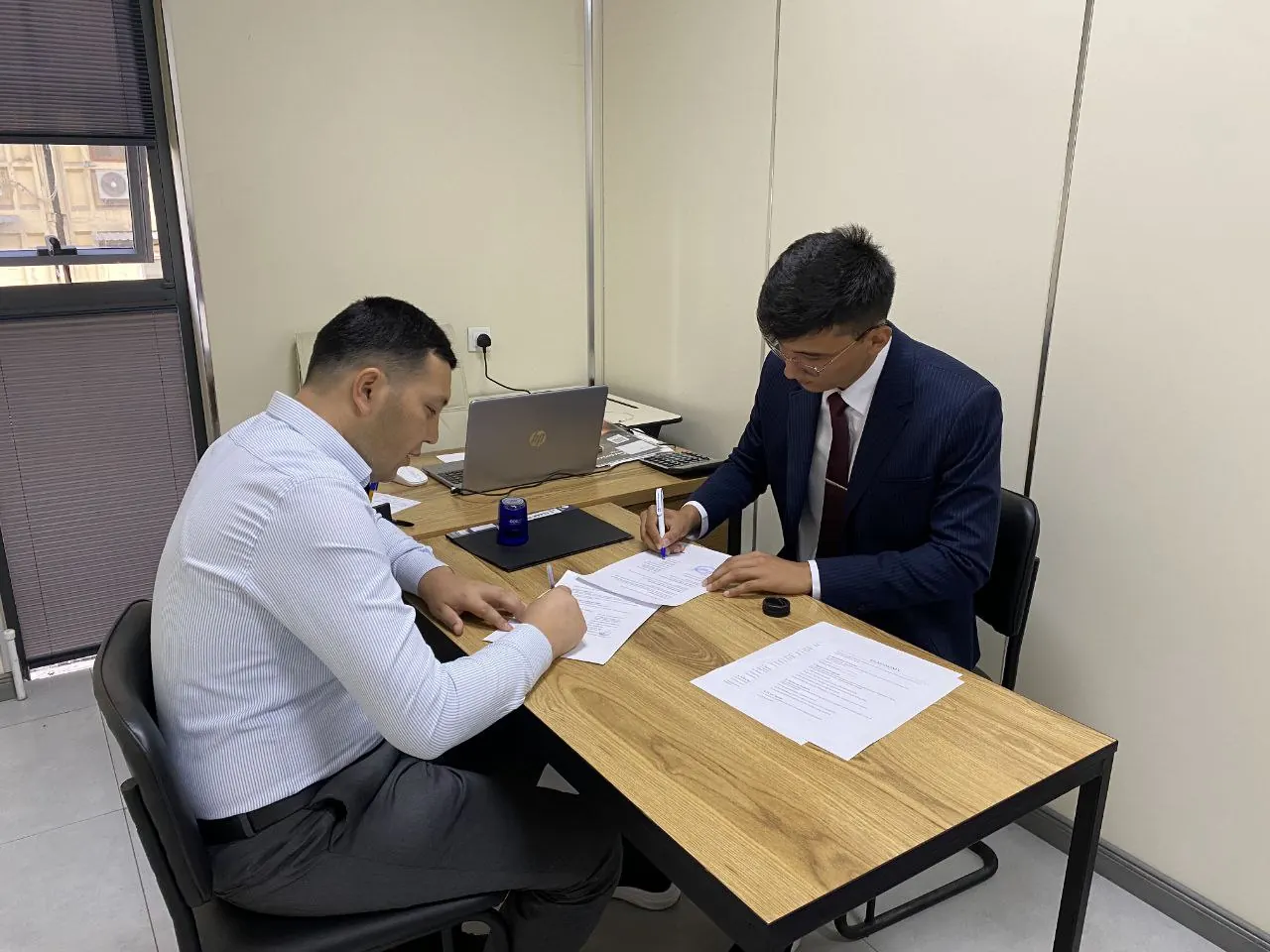 REAL EXAMS and Registan LC representatives signing the partnership agreement at a desk.